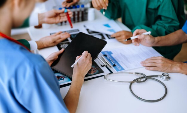 Foto un team medico ha un incontro con medici in camice da laboratorio bianco e abiti chirurgici seduti a un tavolo che discutono di pazienti che lavorano online utilizzando computer nell'industria medica