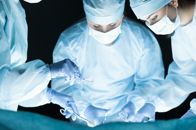 Медицинская бригада выполняет операцию. Группа хирургов за работой в операционной, тона синего цвета