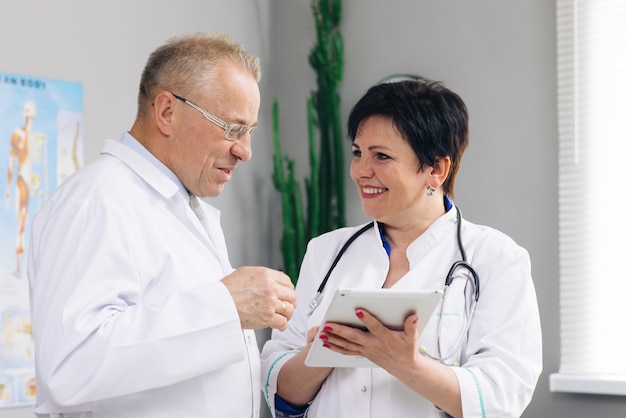 Medical team two old male and young female doctors wear white coats talk, use digital tablet