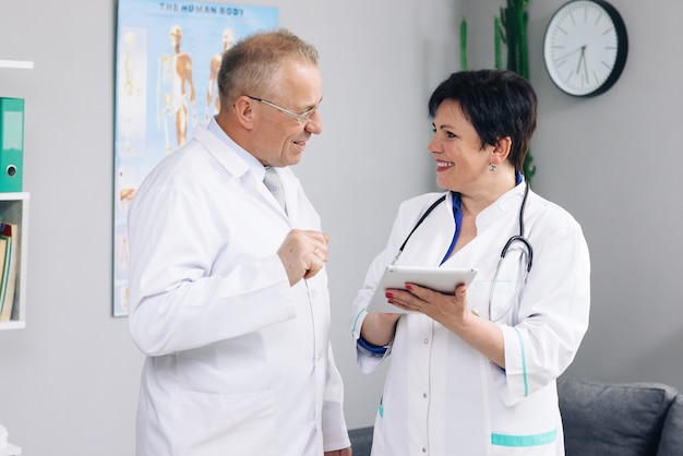 Medical team two old male and young female doctors wear white coats talk, use digital tablet