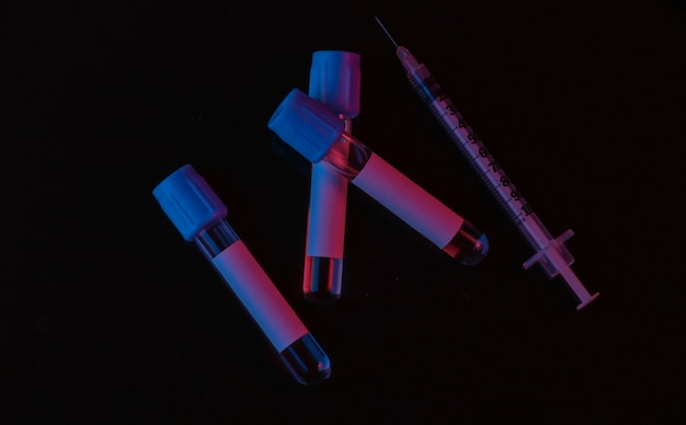 Medical test tubes and syringe on black background with red blue neon light