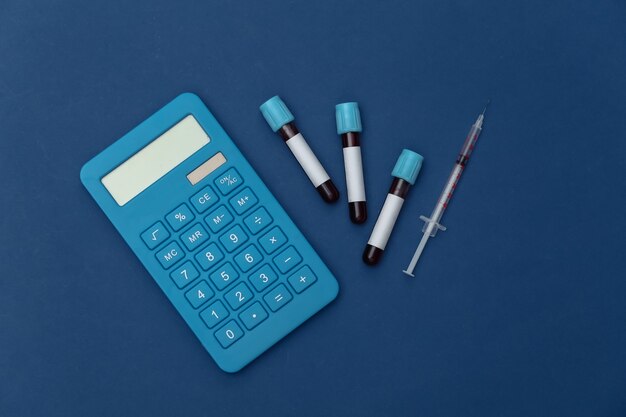 Medical test tubes with blood, syringe and calculator on a classic blue background. Top view