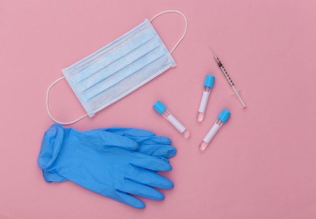 Medical test tubes with syringe and face mask, gloves on pink pastel background. Top view