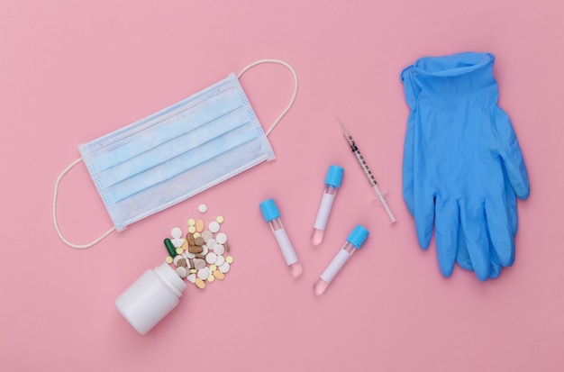 Medical test tubes with syringe, pills and face mask, gloves on pink pastel background. Top view