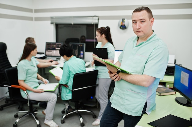 Medical theme .Portrait of male doctor with clipboard against group of doctors meeting in the mri office at diagnostic center in hospital.