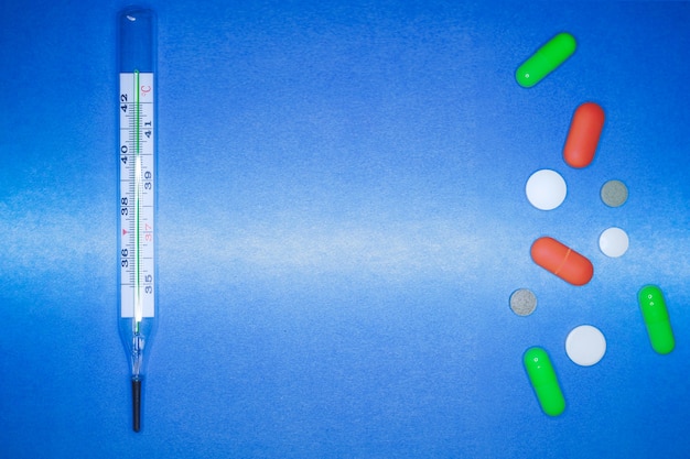 Medical thermometer and color pills on a blue background. healthcare and first aid concept.