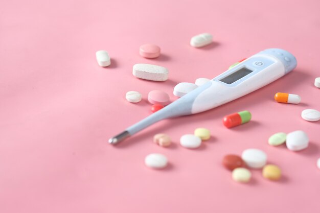 Medical thermometer and pills on pink texture background