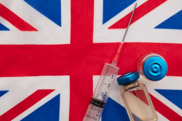 A medical vaccine syringe and vial bottle on a united kingdom union jack flag