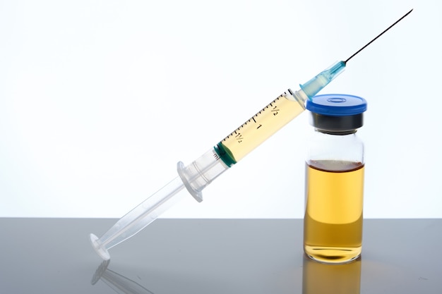 Medical vial vaccine dose and syringe on mirror surface, white backdrop, selective focus