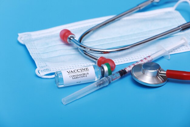 Medical vial with Coronavirus Vaccine COVID-19, syringe, stethoscope and face mask on blue background