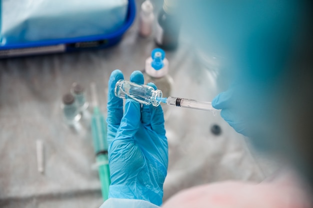 A medical worker in blue gloves takes a vial of vaccine into a syringe