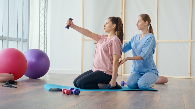 Medical worker helping pregnant woman to do ball exercises