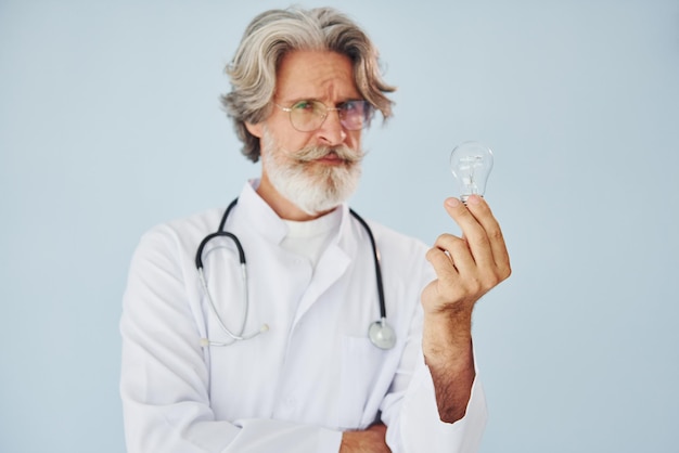 Medical worker holds light bulb in hands Senior stylish modern man with grey hair and beard indoors