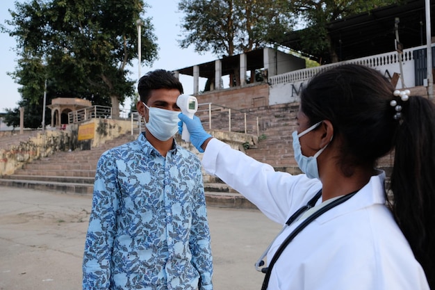 Medical worker monitoring the temperature of an Indian young man with a thermometer