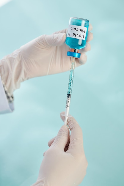 Medical worker in protective gloves holding syringe and vial with COVID-19 vaccine