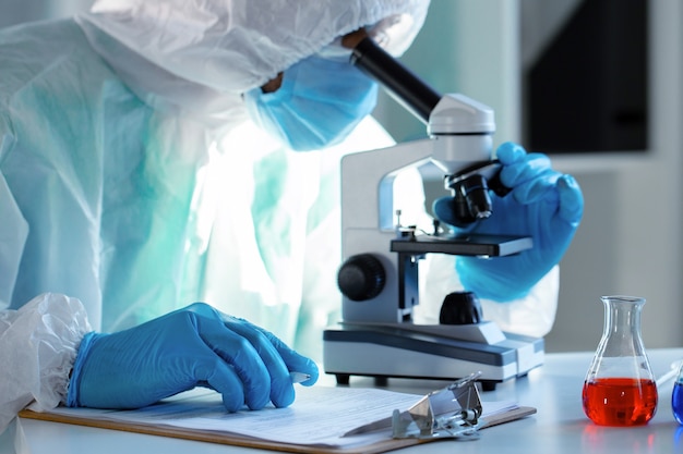 Medical worker in protective gown looking in microscope close up