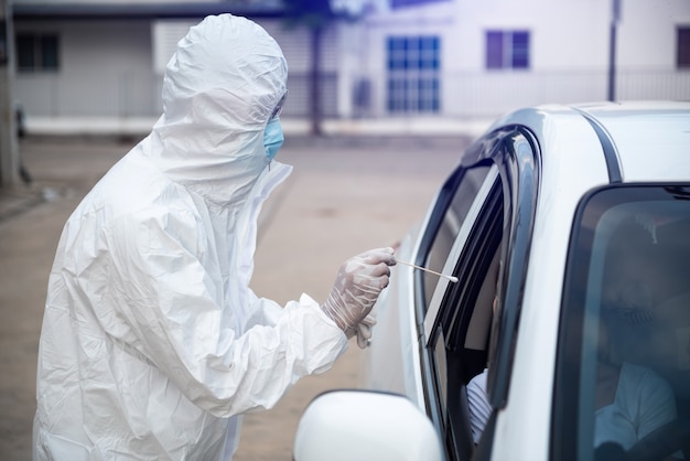 Operatore medico in tuta protettiva donna di screening driver per la secrezione di campionamento per verificare la presenza di covid-19.