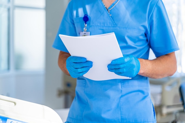 Foto operatore medico uomo serio che tiene analisi mediche indossando uniforme e in piedi nella sala operatoria lavorando in ospedale