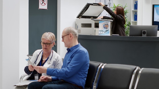 Medical worker sitting at facility reception desk to help\
people with healthcare appointments and patients in waiting room.\
receptionist using checkup visit reports at counter in lobby.