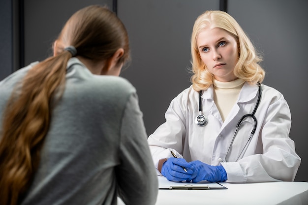 Медицинский работник разговаривает с женщиной в офисе и узнает о симптомах болезни.