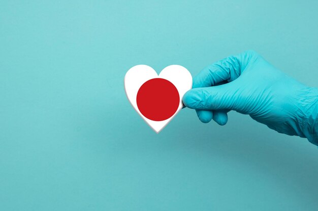 Medical workers hand wearing surgical glove holding japan flag\
heart