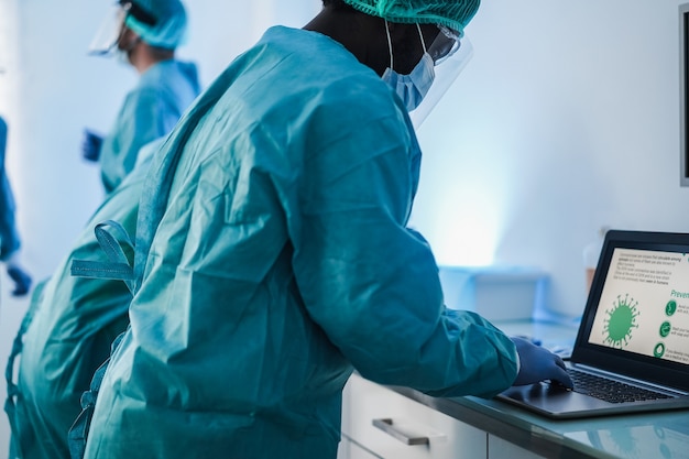 Медицинские работники в костюме хазмат работают с ноутбуком в лаборатории больницы во время вспышки коронавируса