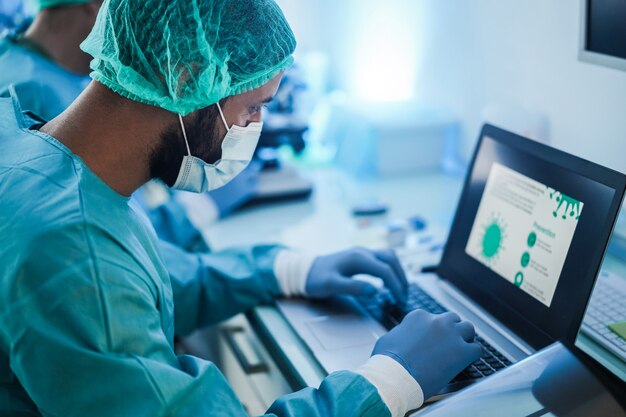 Medical workers in hazmat suit working with laptop computer and microscope inside laboratory hospital during coronavirus outbreak - Focus on doctor head