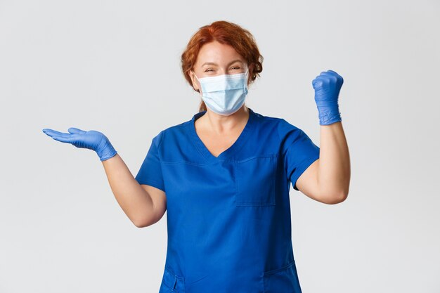 Medical workers,  pandemic, coronavirus concept. Successful and satisfied, happy female doctor, nurse in face mask and gloves, holding something and triumphing, fist pump cheerful.