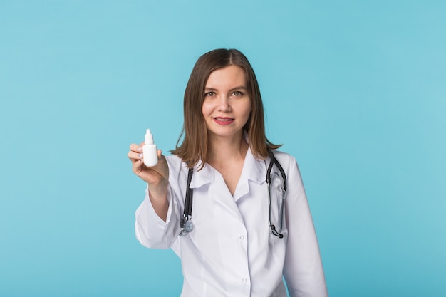 Medicaments and pharmaceutical concept - Young female doctor or pharmacist holding nasal spray on blue background.