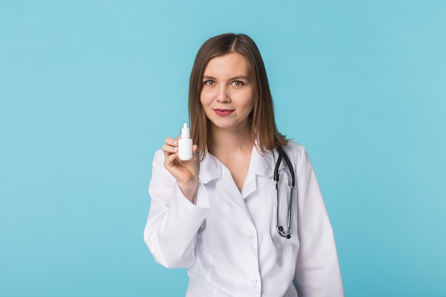 Medicaments and pharmaceutical concept - Young female doctor or pharmacist holding nasal spray on blue wall.