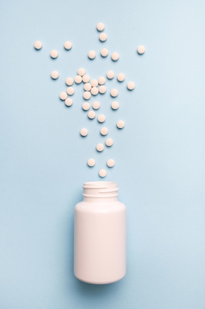 Medicaments pills spilled from a white bottle Healthy and medicine concept on blue background