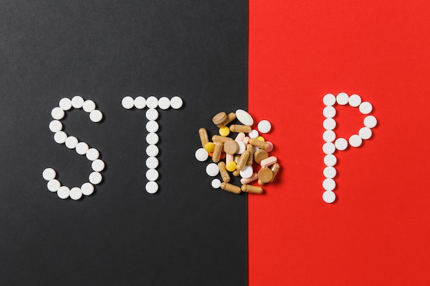 Medicatie witte, kleurrijke ronde tabletten in woord Stop geïsoleerd op zwarte rode achtergrond. Pillenvorm, brief. Concept van gezondheid, behandeling, keuze gezonde levensstijl. Ruimte advertentie kopiëren.