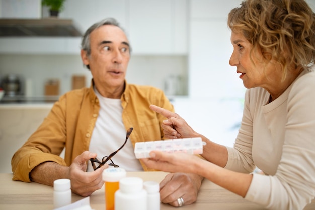 Medicatiesupplementen en behandelingsconcept Senior vrouw die dagelijks pillen geeft aan haar echtgenoot die in het keukeninterieur zit