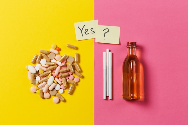 Medication colorful tablets pills arranged abstract, bottle alcohol, cigarettes on yellow pink rose color background