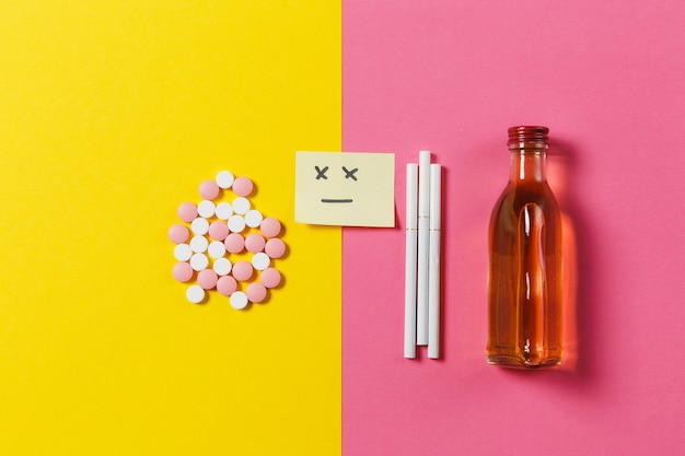 Photo medication colorful tablets pills arranged abstract, bottle alcohol, cigarettes on yellow pink rose color background