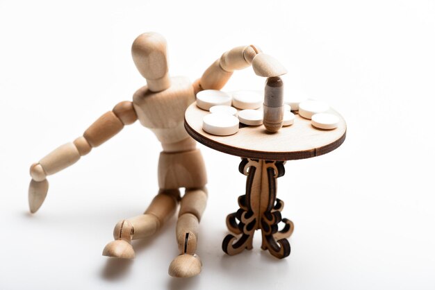 Medication regimen. human wooden dummy near table with\
medicines. tips tackling complex medication regimen. take medicines\
after food. health care and medical treatment. pills on tiny wooden\
table.