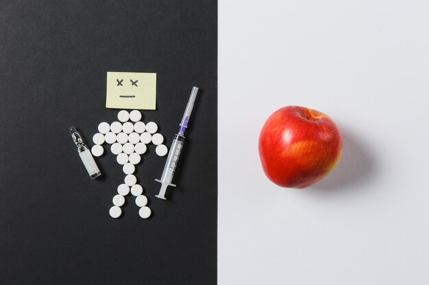 Medication round tablets arranged sad human on white black background. Red apple, ampoule, empty syringe needle, pills design. Treatment, choice, healthy lifestyle concept. Copy space advertisement.