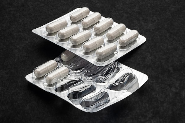 Farmaco pillole di capsule bianche in due blister interi e aperti su sfondo nero