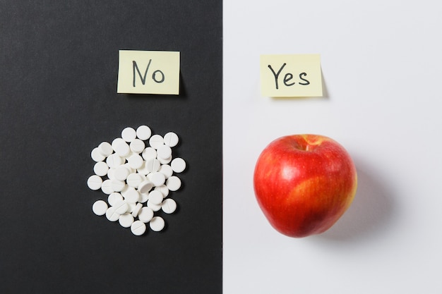 Medication white colorful round tablets arranged abstract on white black background. Red apple, sticker with text yes no, aspirin, pills design. Treatment choice healthy lifestyle concept. Copy space.