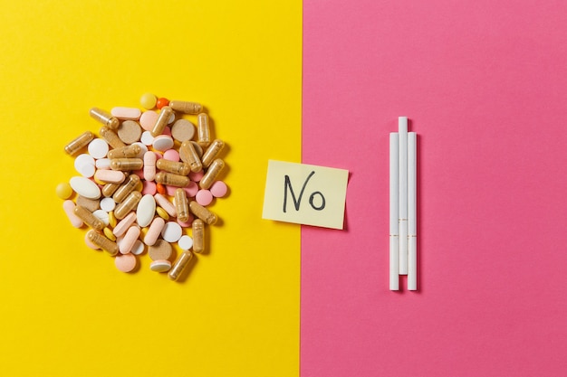 Medication white colorful round tablets pills arranged abstract three cigarettes on yellow color background