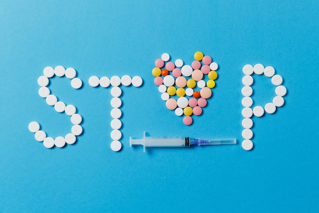 Medication white, colorful round tablets in word Stop isolated on blue background