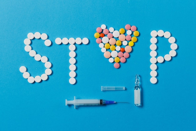 Medication white, colorful round tablets in word Stop isolated on blue background