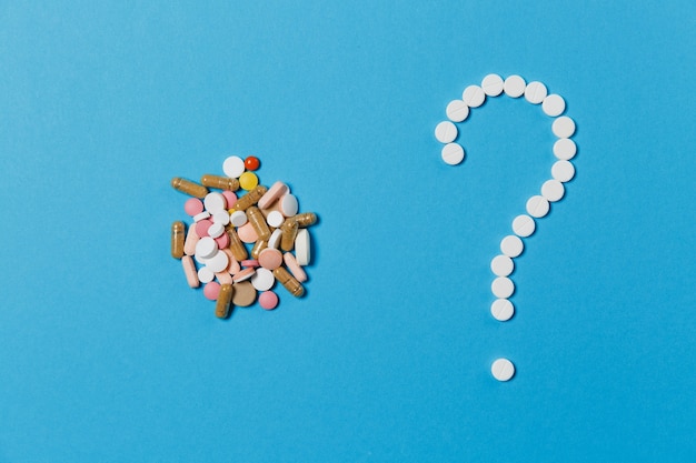 Medication white round tablets arranged in question mark shape isolated on blue color background. Bunch of multicolored pills, colorful sign. Concept of health, treatment, choice, healthy lifestyle.