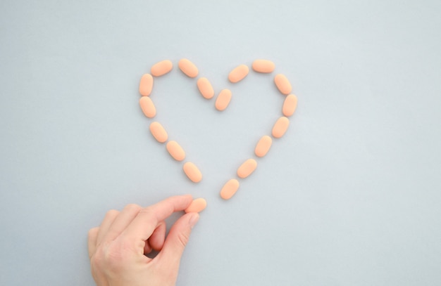 Medications tablets are laid out in the shape of a heart on a blue background. The concept of treatment of heart disease