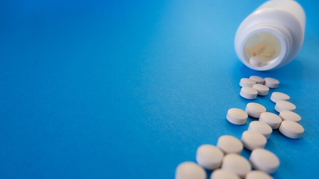 Medicijn- en gezondheidszorgconcept Capsules tabletten verspreid in de buurt van containers op een blauwe achtergrond Plaats voor uw tekst