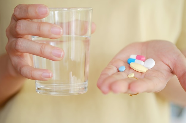 Medicijnen en water in de hand van een vrouw om te eten om ziekte te behandelen. Gezondheidszorgconcept.