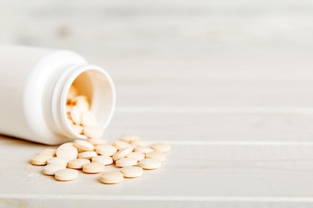 Medicijnfles en witte pillen die op een lichte achtergrond worden gemorst Geneesmiddelen en voorgeschreven pillen liggen plat op de achtergrond Witte medische pillen en tabletten die uit een medicijnfles worden gemorst