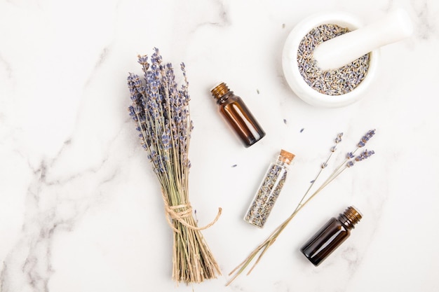 Medicinal lavender flowers and essential oil in medical bottles on a marble table top view flat styling natural medical cosmetics