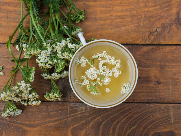 Medicinal plant yarrow, a mug with a decoction of yarrow flowers on a wooden background