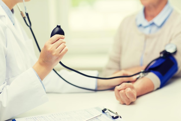 medicine, age, health care and people concept - close up of doctor with tonometer checking senior woman blood pressure level at hospital